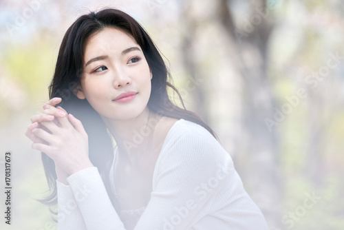 Young Asian female sitting on park bench surrounded by cherry blossoms in spring