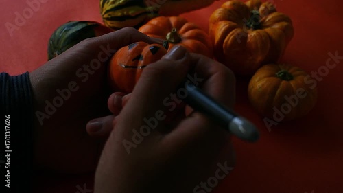 Cozy autumn scene of hands painting some miniature pumpkins, gourds with a marker, highlighting the festive atmosphere and creativity.