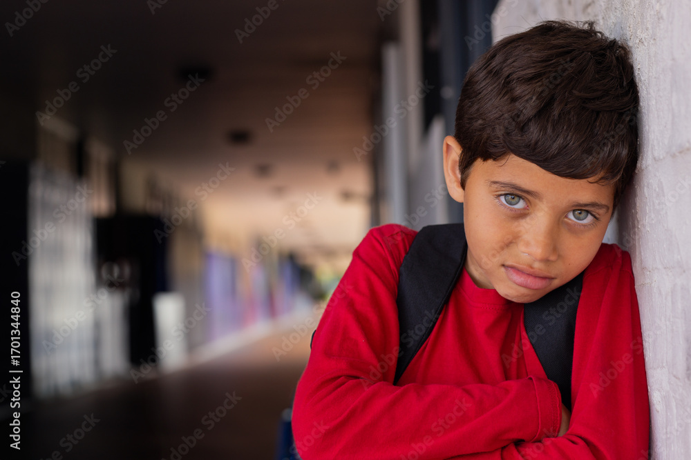 Fototapeta premium School hallway, young boy in red shirt leaning against wall, looking thoughtful, copy space