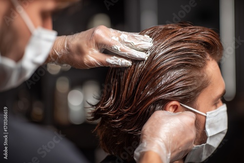 Back view of male model in salon chair with stylist applying rich brown hair dye, soft lighting and blurred contemporary salon background, professional haircare and styling concept