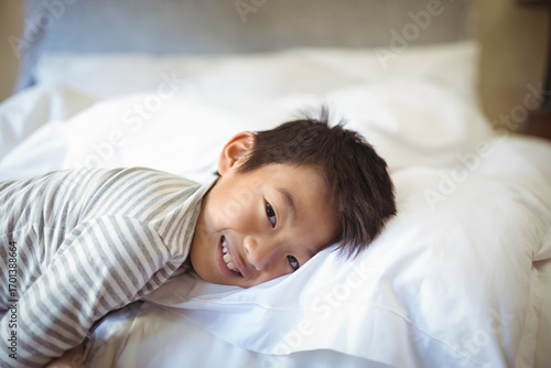 Asian boy lying in bedroom wearing striped pajama top, smiling and resting head on white pillow