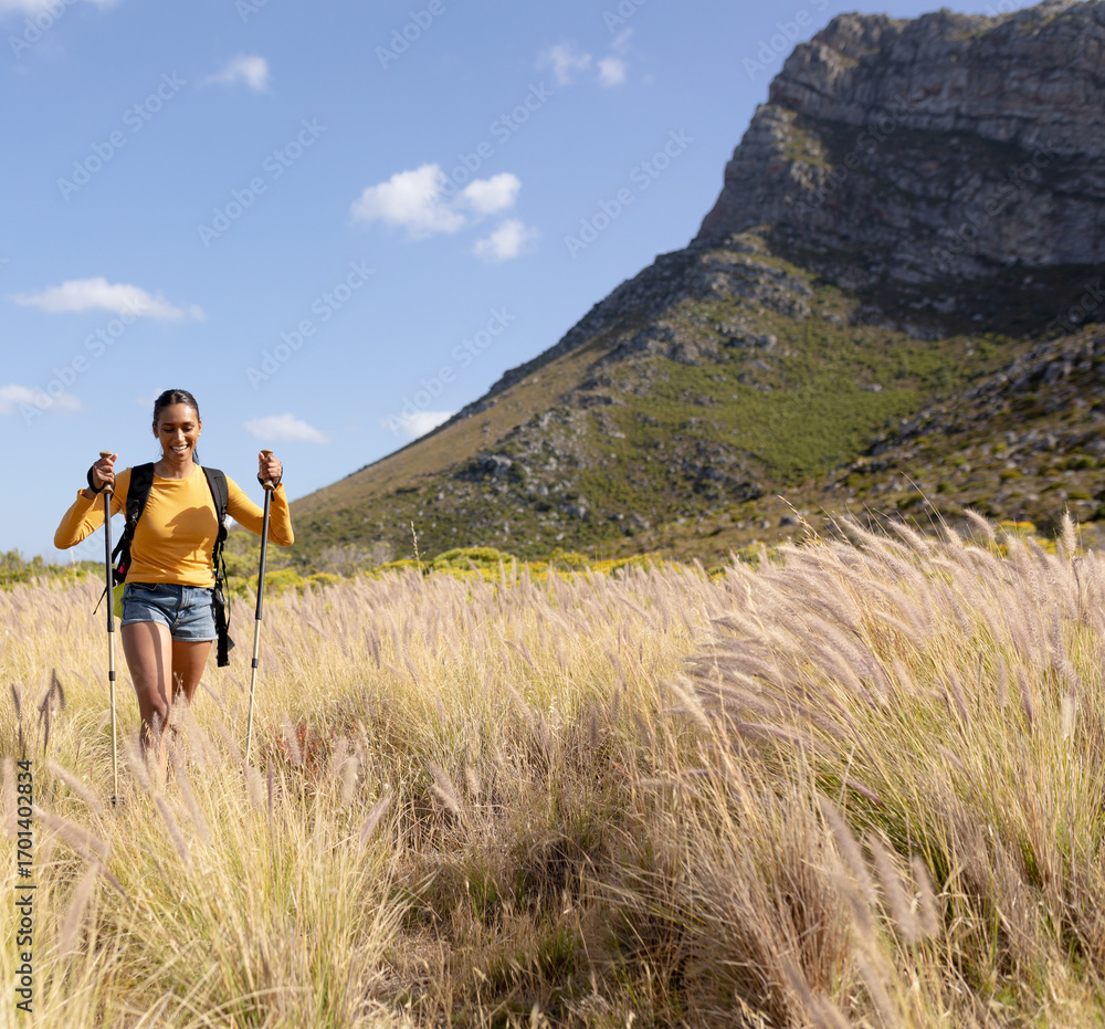 Woman hiking with trekking poles in scenic mountain landscape, enjoying nature, copy space