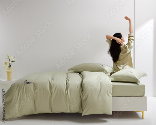 Woman stretching in bed with soft green bedding and pillows, enjoying a cozy morning atmosphere.