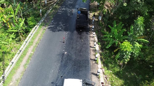 Aerial view of asphalt road repair with trial compaction process, testing surface quality before final paving. Infrastructure construction footage