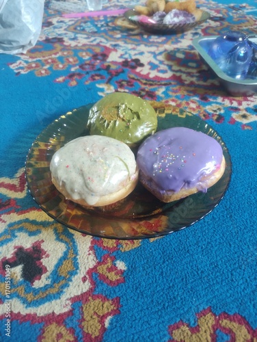 Three donuts on a plate placed on a blue carpet, sweet food with colorful decoration