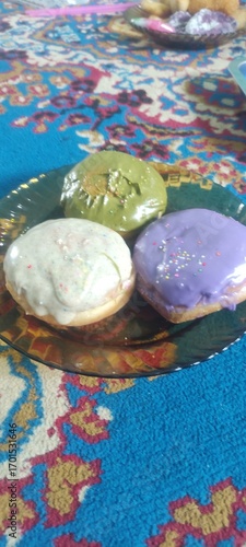Three donuts on a plate placed on a blue carpet, sweet food with colorful decoration