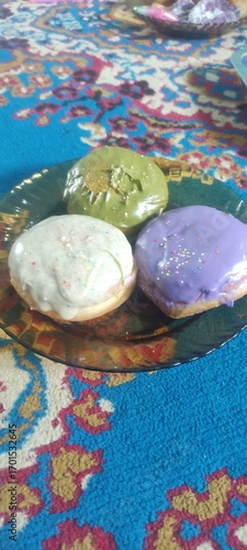 Three donuts on a plate placed on a blue carpet, sweet food with colorful decoration