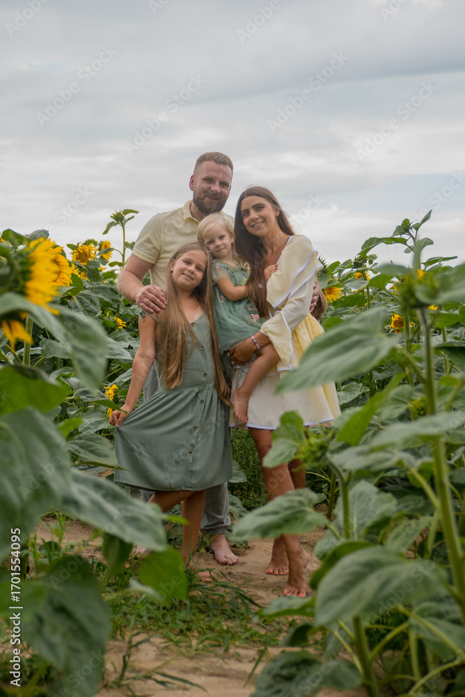 Fototapeta premium A family with two daughters in a sunflower field, looking at the camera. Concept of growing crops, agriculture, farming, autumn, harvesting