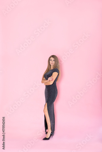 Valokuvatapetti A woman in a black elegant dress with a high slit and high heels on a pink background