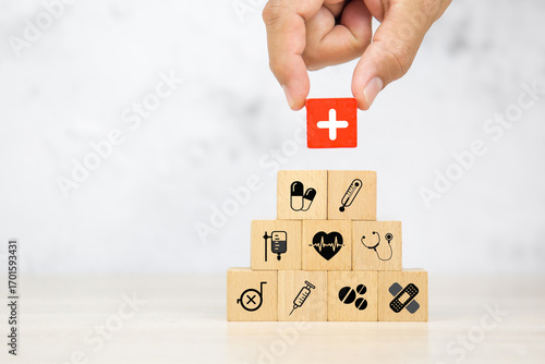 Hand chooses wooden toy block stack with health insurance icons for wellness medical care and healthy for family safety insurances plan or personnel sickness illness treatment concept.
