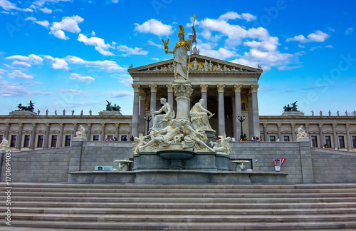 A majestic view of the historic Austrian Parliament Building and the magnificent Pallas Athene Fountain under a vibrant blue sky in Vienna