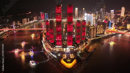 Drone aerial video of Chongqing at night showing illuminated skyscrapers, glowing skyline, colorful reflections on the river, above vibrant boats and traffic moving in cinematic view slow motion