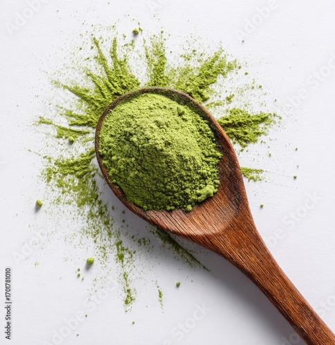 Wooden spoon filled with green matcha powder, scattered on white surface