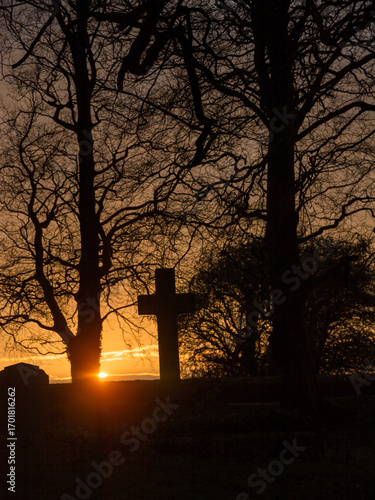 Ancient cross tombstone silhouetted at sunset