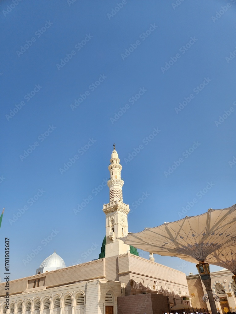 Fototapeta premium View of Al-Masjid an-Nabawi in Madinah Al Munawwarah, Saudi Arabia. The image features the iconic green dome and minarets. Intricate architectural details of the mosque are visible, including ornate