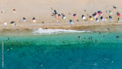Aerial drone view of sandy beach and turquoise sea waves with people sunbathing, swimming and relaxing, holiday vacation concept, Antalya Konyaalti beach, Turkey