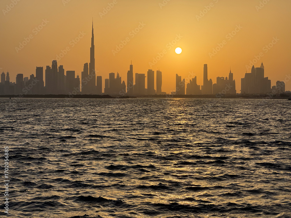 Obraz premium Dubai skyline silhouette panoramic view at sunset with orange sky and Creek waterfront, high resolution cityscape background