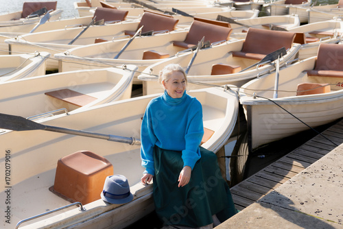 Gray-haired woman in a blue sweater against the background of boats, a lake and a forest in the Versailles park