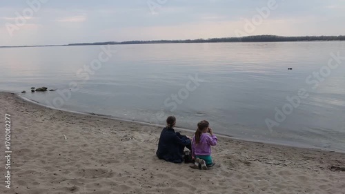 family mom and daughter is eight years old drinking tea and eating sandwiches sitting on the sand near the river on a spring day.  Family leisure with kids at spring.