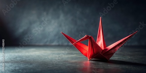 Red paper crane origami on a dark textured background with shadows