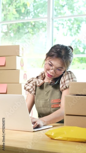 Young Asian female entrepreneur manages online business orders from home using smartphone, laptop and e-commerce work package.