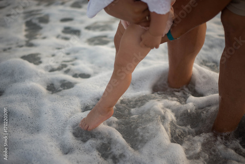 Father holding baby by the sea, playing together in the waves. Tender family moment full of love, care, and joy. Concept of fatherhood, childhood, bonding, and vacation lifestyle outdoors.