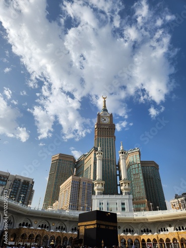 The image shows the Abraj Al Bait Towers, specifically the central tower known as the Makkah Clock Tower, in Mecca, Saudi Arabia. The scene captures pilgrims gathered in the courtyard of the Masjid al