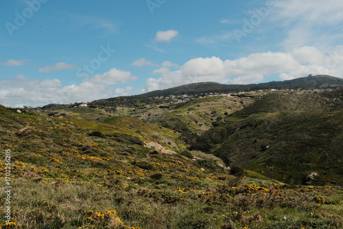 Lush green hills and rugged terrain with blue sky and scattered clouds in Cabo da Roca Sintra Portugal natural landscape with vegetation from scenic hiking trail