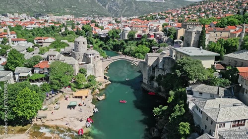 4K aerial drone zoom-out of Old Bridge in Mostar, Bosnia and Herzegovina, along the Neretva River, revealing the Koski Mehmed Pasha Mosque and the historic old town during daylight.  