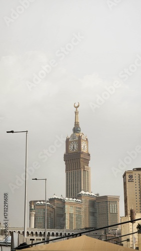 The image shows the Abraj Al Bait Towers, specifically the central tower known as the Makkah Clock Tower, in Mecca, Saudi Arabia. The scene captures pilgrims gathered in the courtyard of the Masjid al
