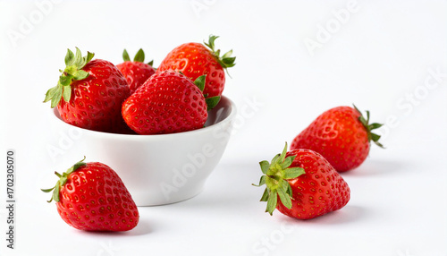 bright red berry fruits are featured in a still life. several of the fruits sit nestled in a small, bright white bowl, while others are placed nearby on the surface