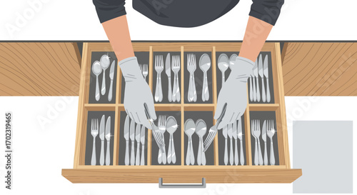 Person's hands arranging cutlery in a wooden drawer, organizing the silverware