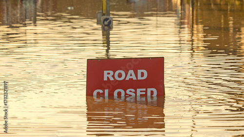 Tableau sur toile A 'Road Closed' sign partially covered in flood water lit by the evening sun
