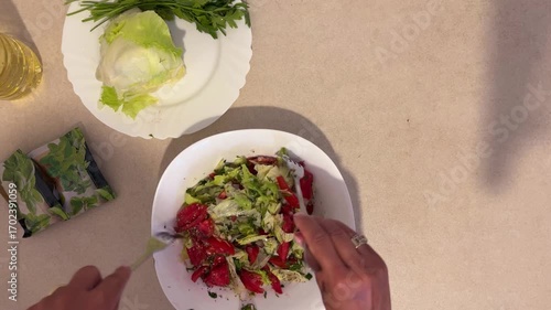Hands mixing a salad on a plate, top view