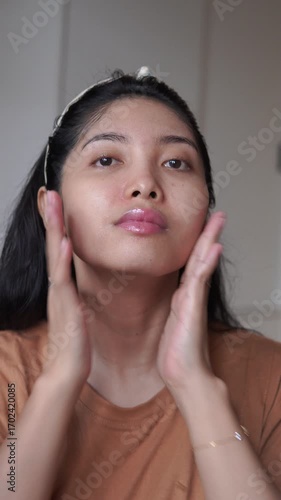 Calm young Asian woman is removing her make up using cleansing oil, maintaining healthy skin.