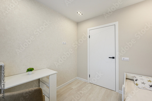 Bright room featuring a desk, white door, and light wood flooring. Minimalist design with neutral tones