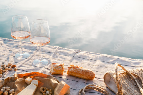 Two glasses of rose wine with cheese and nuts on a pier at sunset.
