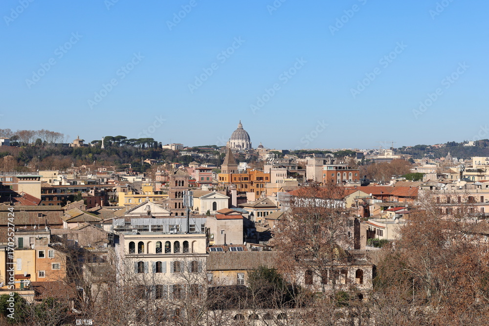 Fototapeta premium A panoramic view of Rome with historic rooftops and the dome of St. Peter’s Basilica rising in the background under a clear blue sky.
