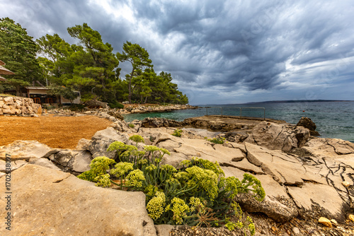 Tara Beach, Rab, sun umbrellas on the shore of the Adriatic Sea, cloudy, threatening sky, azure water