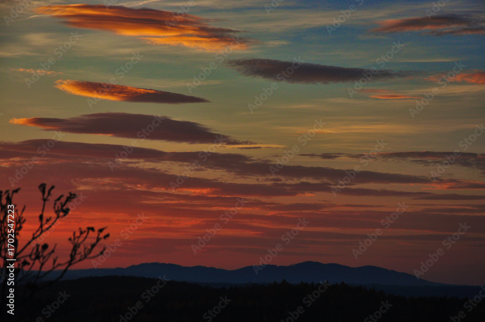 Fototapeta premium Radogost - widok z wieży. Urzekająca scena zachodu słońca ze złotymi odcieniami rozpościerającymi się po niebie, gdy słońce chowa się za odległymi wzgórzami.