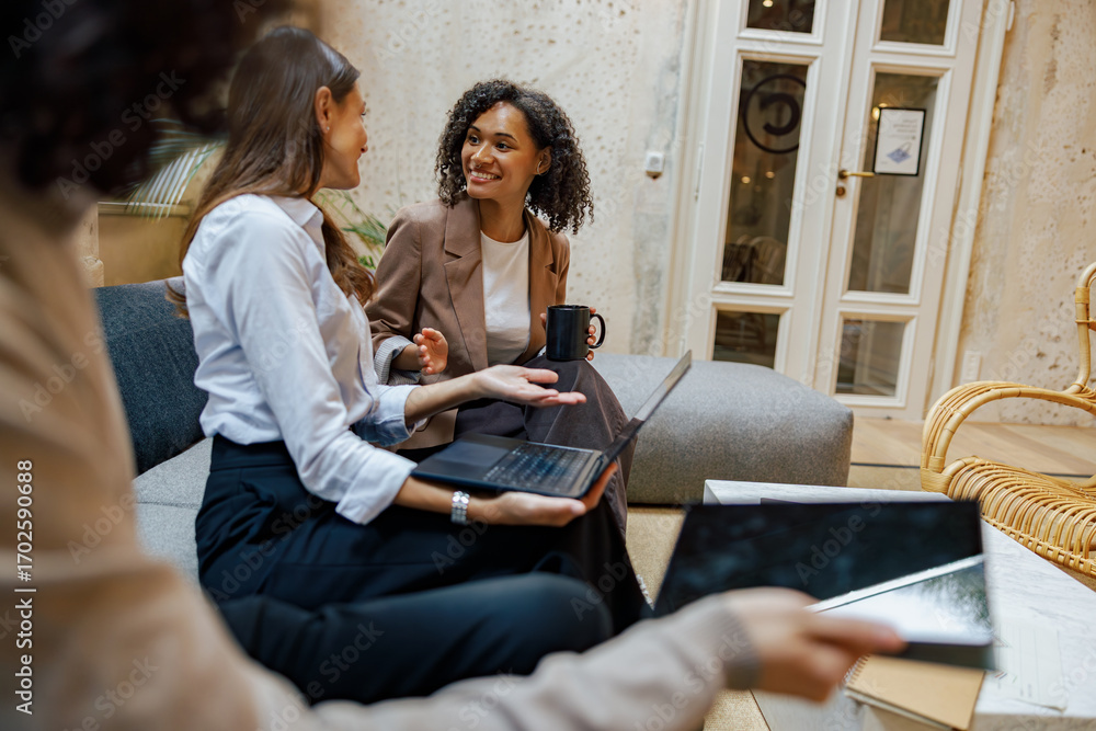 Fototapeta premium In a modern office, two professional women are engaged in an animated discussion while using their devices