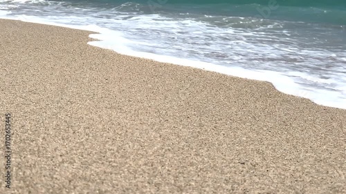 Waves gently washing onto a sandy beach. Serene coastal scene with turquoise ocean water, golden sand on a peaceful summer day