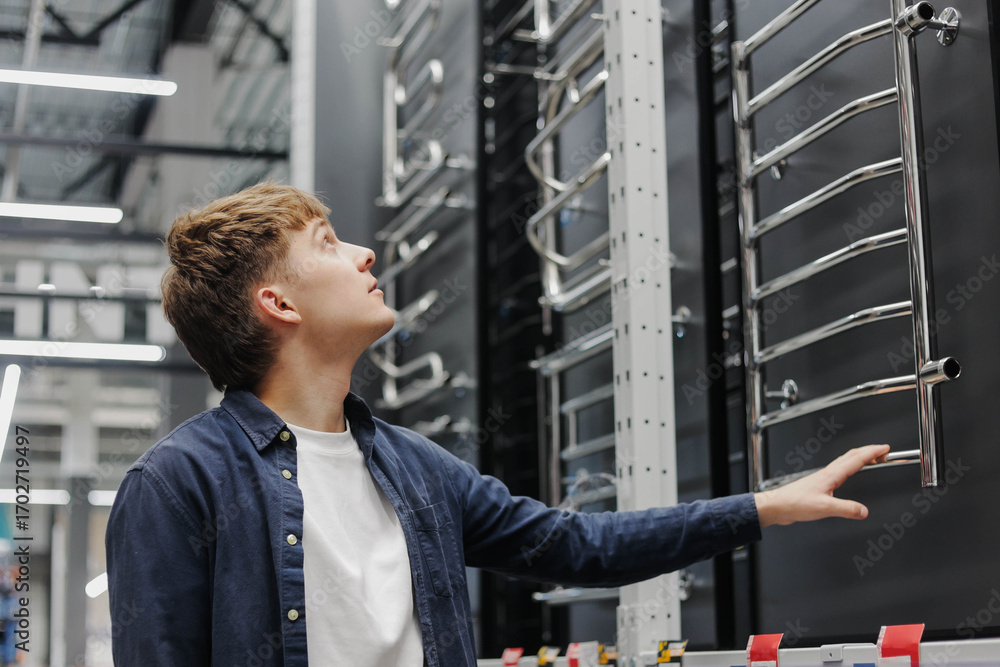 Fototapeta premium Young man choosing towel warmer in hardware store