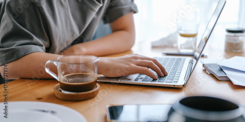  Gen Z woman working from home at cozy kitchen table with laptop and phone. Digital nomad lifestyle, mindfulness, remote work, balance, mental calm and modern freelancing