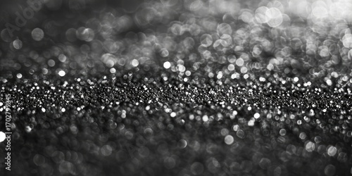 Monochromatic bokeh photograph featuring a dense cluster of out-of-focus light points, creating a glittering, textured effect, with darker tones at the edges