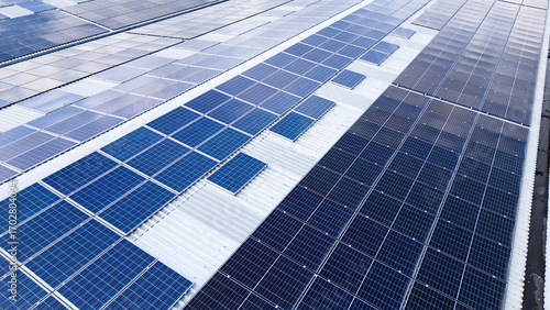 Aerial drone view of solar panels installed on a warehouse roof in an industrial park, showcasing renewable energy and sustainable power generation.