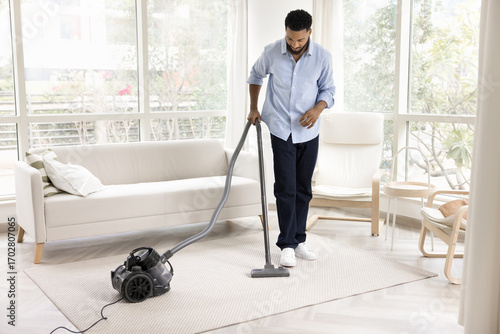 Wallpaper Mural Young male vacuuming carpet on floor with washing vacuum cleaner Torontodigital.ca