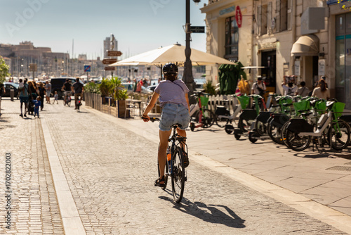 Jeune femme à vélo sur la piste cyclable de la Canebière en direction du Vieux-Port de la ville de Marseille, vue de dos portant un casque, un T-shirt et un short en jean