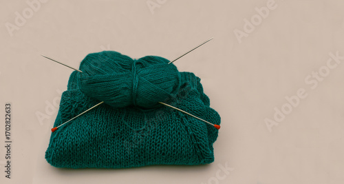 Fotografie Knitted item in green merino wool yarn with knitting needles on neutral backgrou