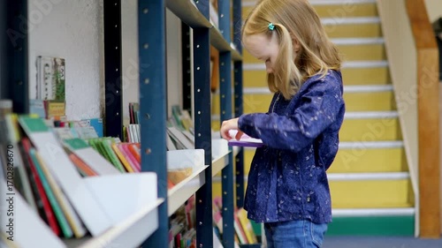4 year old girl in municipal library and reading a book. Literature for children